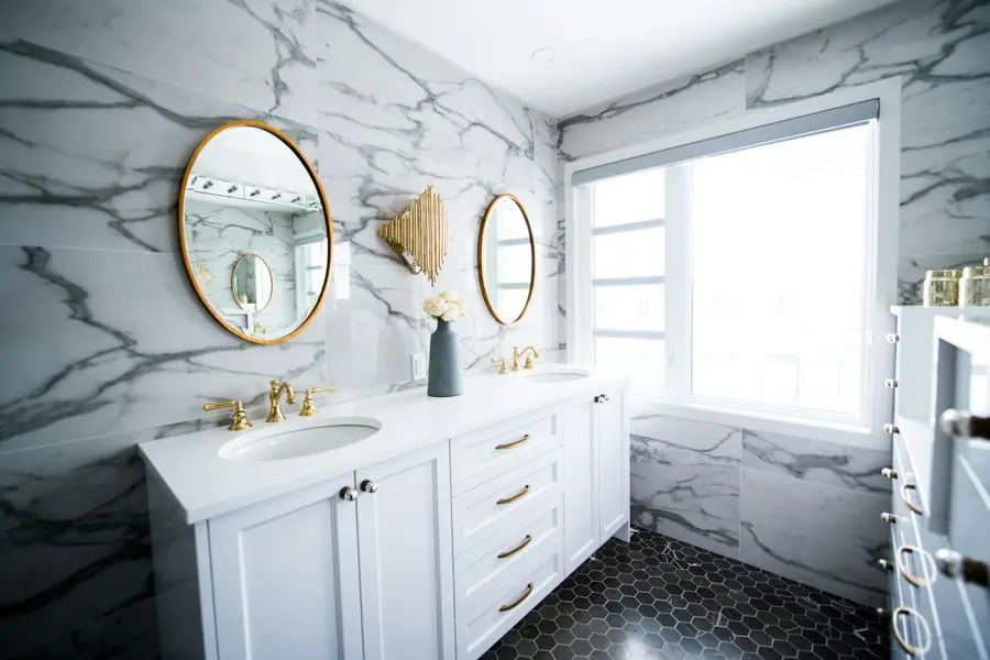 Double-vanity bathroom remodel with marble walls and gold fixtures