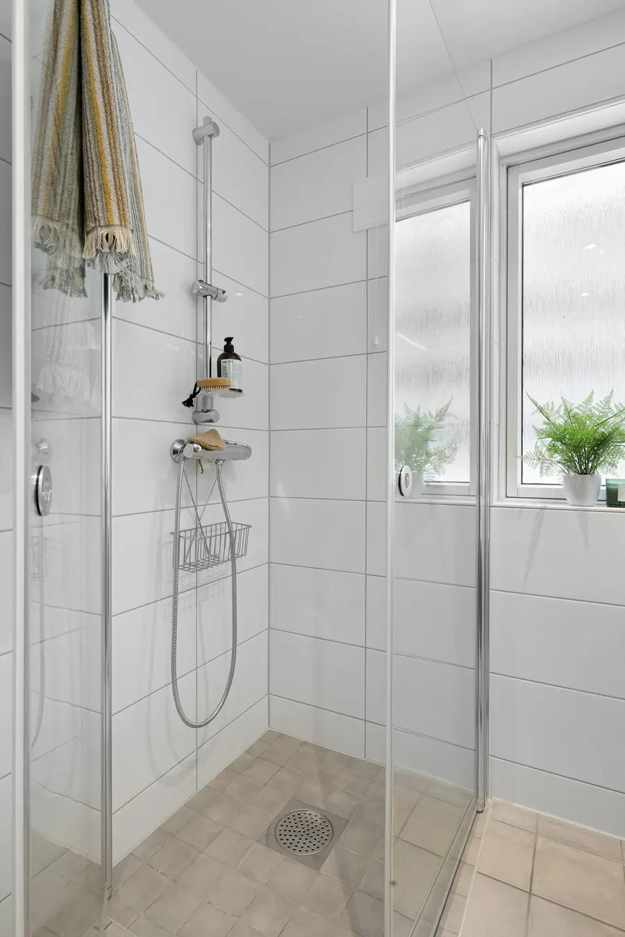 Bright walk-in shower with white tile and a glass panel