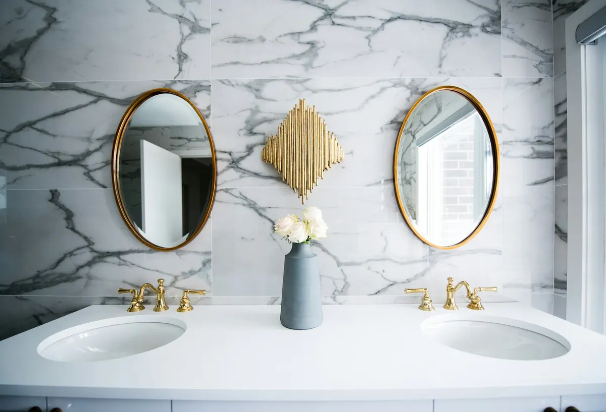 Double vanity with marble wall, brass faucets, and round mirrors
